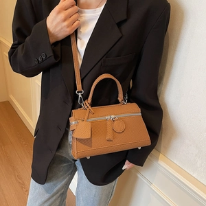 Brown leather handbag with silver zipper and shoulder strap worn by a model in a suit