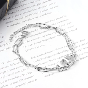 Close-up of double-layer silver chain bracelet with handcuffs pendant and paper background