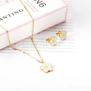 Détail d'un ensemble de bijoux fleurs en émail blanc avec collier doré et boucles d'oreilles