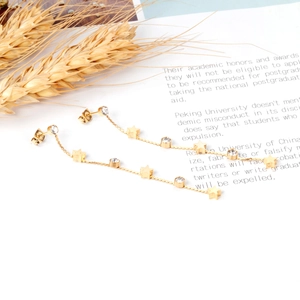 Détails de boucles d'oreilles pampilles dorées avec étoiles et cristaux sur fond blanc