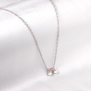 Close-up of rainbow and cloud pendant on silver chain over white satin fabric