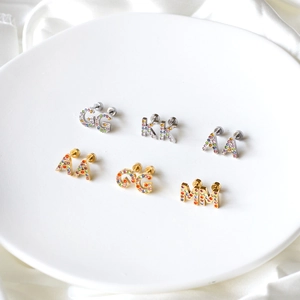 Macro detail of letter earrings G, K, A, M with colorful zircon inlays on white silk
