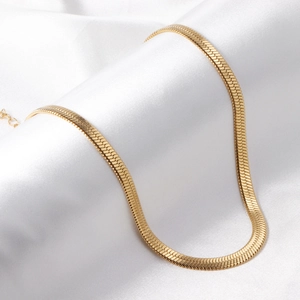Detailed close-up of a gold flat snake chain necklace on white satin fabric texture