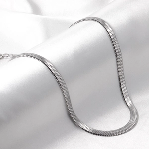 Detailed close-up of a silver stainless steel snake bone chain on white silk fabric