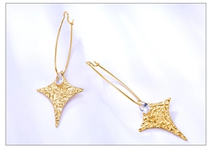 Detalle macro de pendientes de estrella dorada con textura de lava y circón en seda