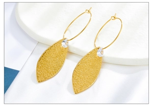 Detalle de pendientes de hoja dorada con textura floral y circonita sobre base de piedra