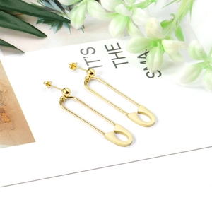 Detailed view of gold safety pin earrings on a white card with green leaf accents