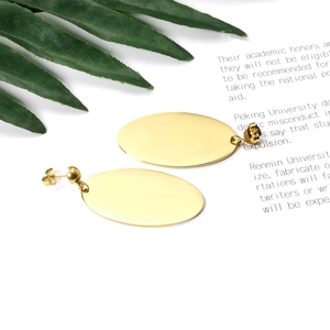 Close-up of elegant gold oval drop earrings with a polished mirror finish on white background