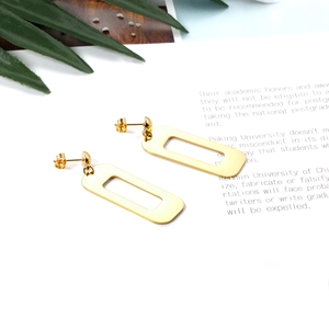 Detail of minimalist gold-plated rectangular hollow earrings on a white background