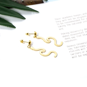 Close-up of golden S-shaped wave drop earrings with polished surface and sphere studs