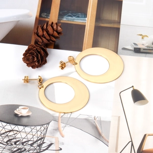 Flat round gold stainless steel hollow earrings displayed with pine cones on a magazine
