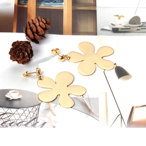 Close-up of gold matte finish flower earrings on white background with pine cones