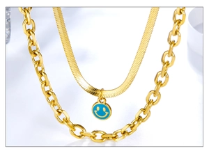 Close-up of golden layered necklace with sleek snake chain and blue smiley face pendant