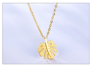 Detail of gold hollow monstera leaf pendant necklace on light blue background
