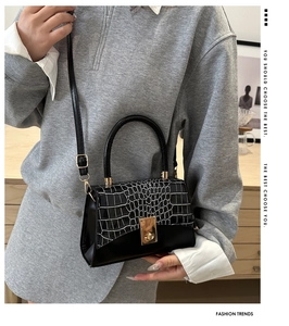 Detail of glossy black crocodile-patterned handbag with metal lock and leather handle