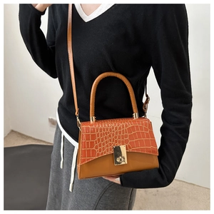 Detail of orange crocodile pattern texture and golden swivel lock on a crossbody bag
