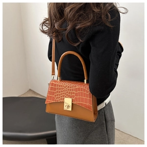 Detail view of crocodile pattern flap and gold twist lock on stylish orange crossbody bag