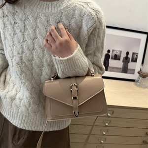 Minimalist beige crossbody bag with gold buckle detail held by a model in knitwear