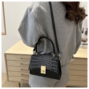 Detail of black and white handbag with crocodile texture and golden clasp on model