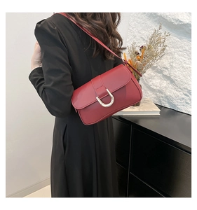 Detail of dark red leather shoulder bag featuring a prominent gold U-shaped metal buckle