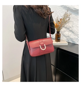 Close-up of a burgundy leather crossbody bag with a large gold horseshoe buckle detail
