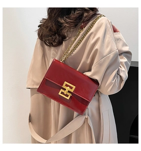 Model wearing a red patent leather square crossbody bag with gold H-clasp and chain strap
