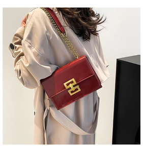 Detail of red patent leather square bag with gold lock and chain strap on a model