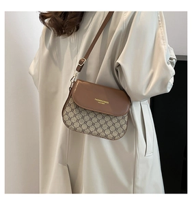 Detail of crossbody saddle bag in brown leather and monogram fabric worn with a trench coat