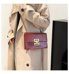 Detail of burgundy textured patent leather crossbody bag with golden chain and lock