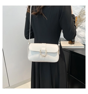 Close-up of white leather crossbody bag featuring a golden horseshoe buckle on a model