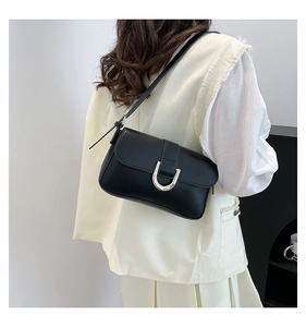 Detail view of the black matte shoulder bag with a silver U-shaped metal buckle on the flap