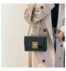 Detail of black leather crossbody bag with gold geometric buckle and chain strap