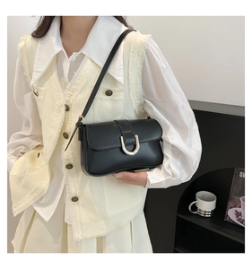Close-up of black crossbody bag with gold horseshoe buckle worn by a model in a cafe