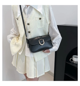 Detail of a minimalist black leather crossbody bag featuring a golden horseshoe metal clasp