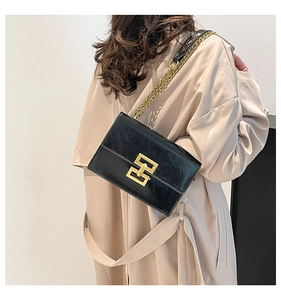 Detail of black leather crossbody bag with gold H-buckle worn over a beige trench coat