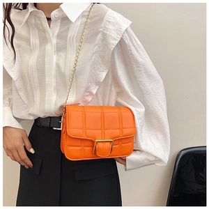 Close-up of orange quilted crossbody bag with gold chain strap on model in white shirt
