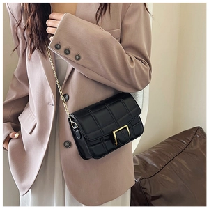 Close-up of black quilted shoulder bag featuring gold buckle and chain strap on a model