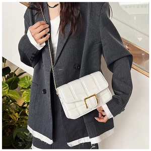 Close-up of a white quilted crossbody bag featuring a gold square clasp and chain strap