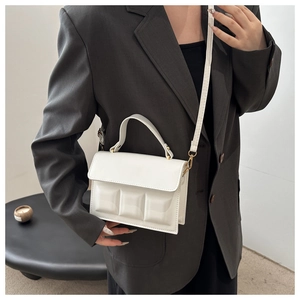 Close-up of white crossbody bag with 3D cube embossed texture and metallic gold hardware