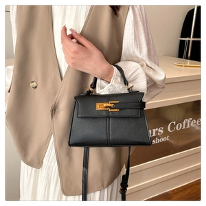 Dettaglio borsa in pelle martellata nera con chiusura dorata su abito bianco