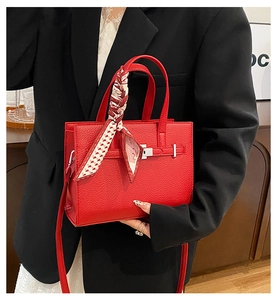 Gros plan d'un sac à main rouge en cuir grainé avec foulard décoratif sur la poignée