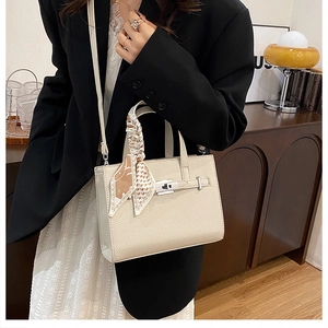 Détail du sac crème avec foulard en soie sur la poignée et fermoir argenté tournant