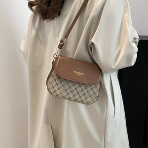Classic brown monogram crossbody saddle bag with leather flap worn with a beige trench coat