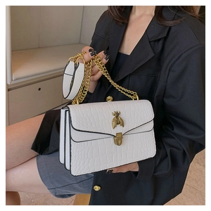Détail d'un sac blanc à motif crocodile avec un fermoir en forme d'abeille dorée