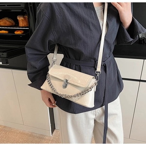 Sac à rabat chic en cuir verni blanc crème avec chaîne argentée porté par le mannequin