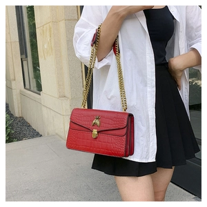 Détail du sac bandoulière rouge motif crocodile avec boucle abeille dorée et chaîne