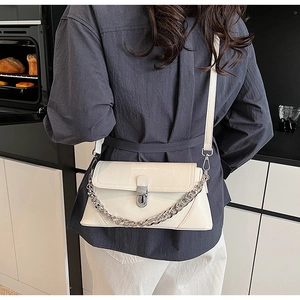 Détail du sac à bandoulière en cuir verni crème avec chaîne argentée et fermoir métallique