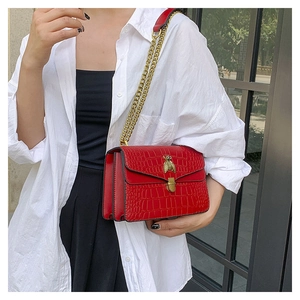 Détail d'un sac bandoulière rouge effet crocodile avec fermoir abeille doré et chaîne