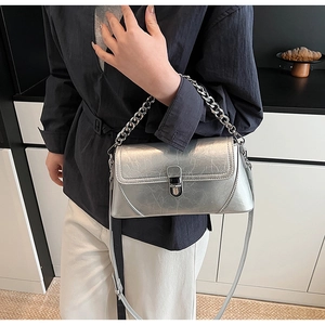 Gros plan sur la chaîne argentée et la texture craquelée du sac à bandoulière chic