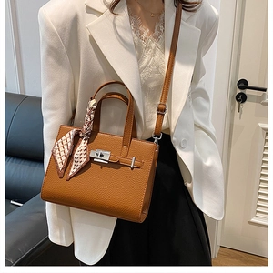 Détail d'un sac à main en cuir marron avec foulard en soie sur la poignée et fermoir métal